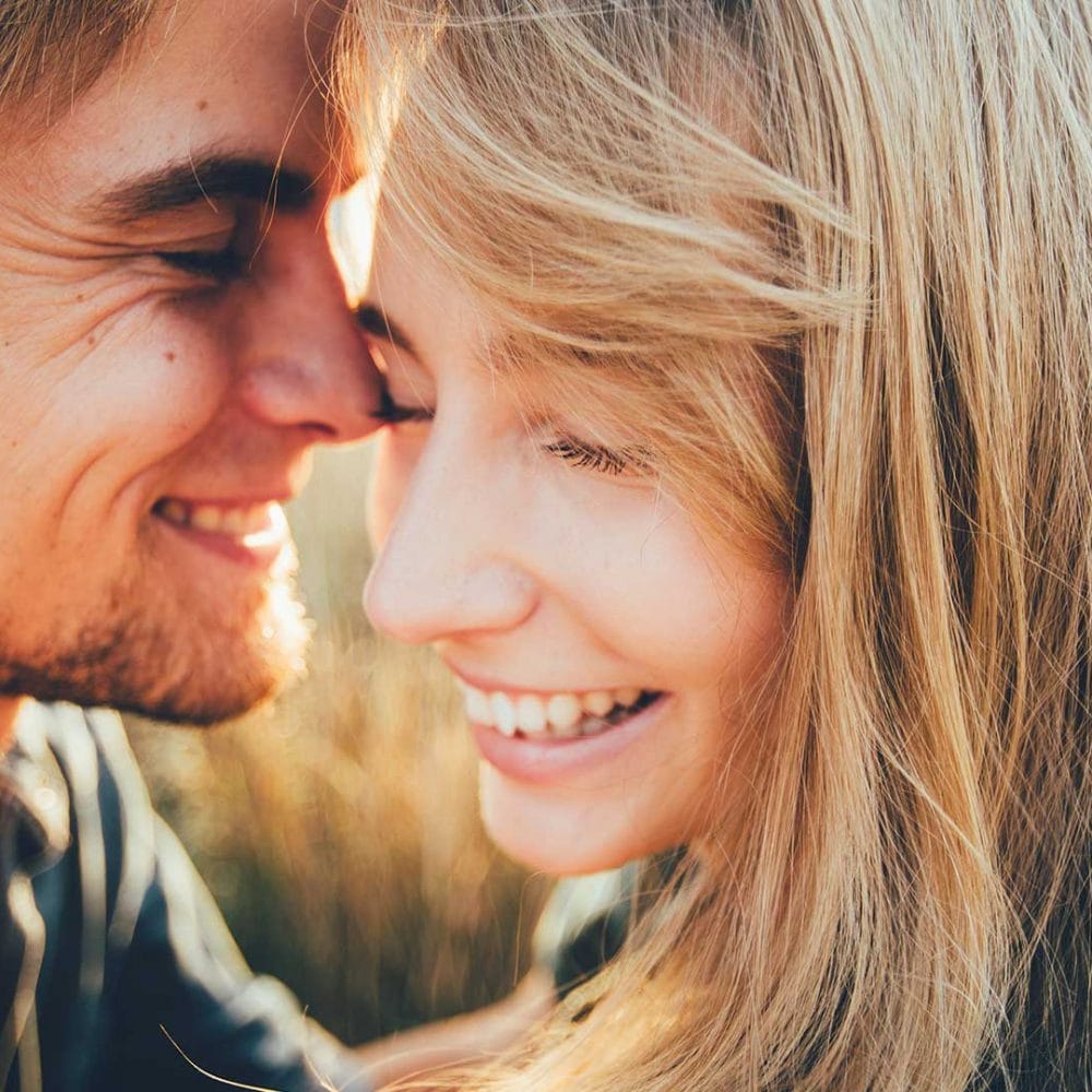 Couple smiling happily and standing close together in a close-up.