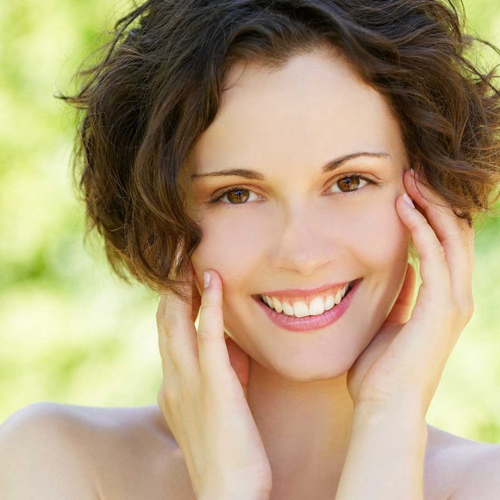 Beautiful woman with clear skin and a joyful smile, hands on face.
